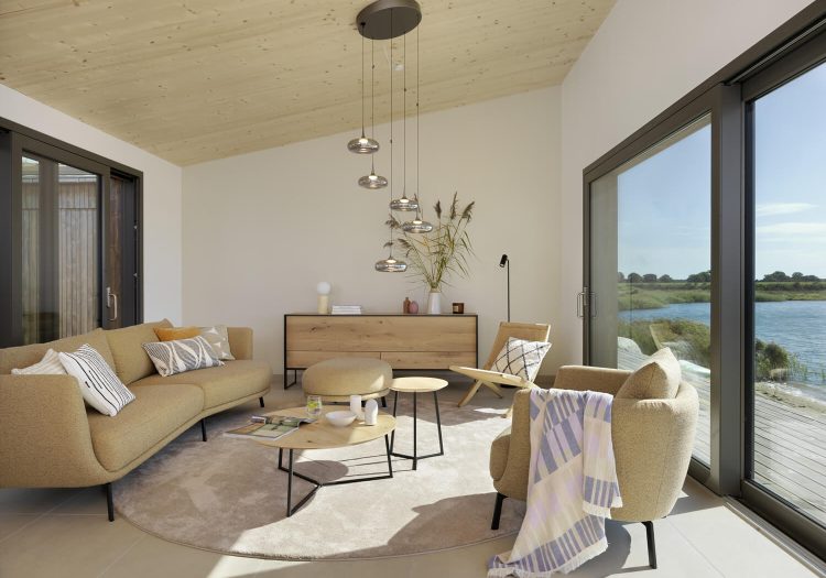 Gemütliches Wohnzimmer mit hellen Sofas, Designlampen und Blick auf den See durch bodentiefe Fenster.
