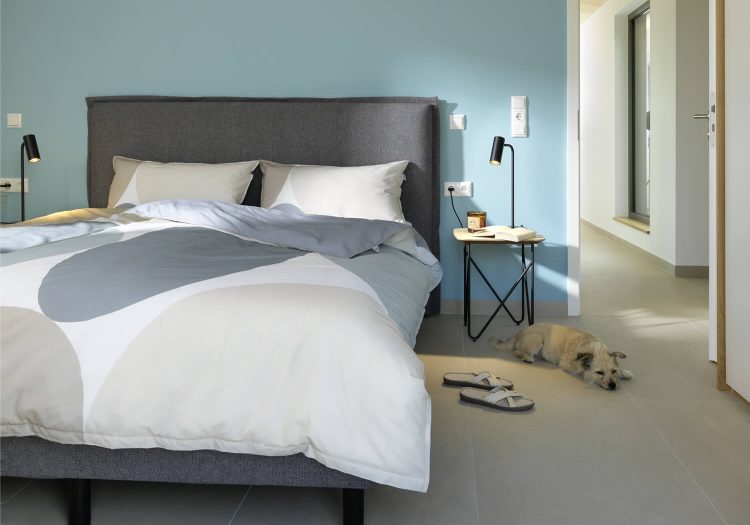 Schlafzimmer mit Doppelbett, blauer Wand und Blick in den Flur, Hund liegt auf dem Boden.